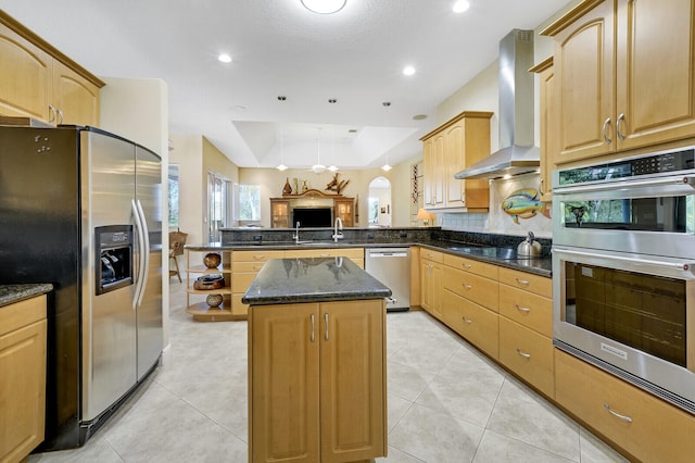 kitchen featuring kitchen peninsula, wall chimney exhaust hood, stainless steel appliances, dark stone countertops, and a kitchen island