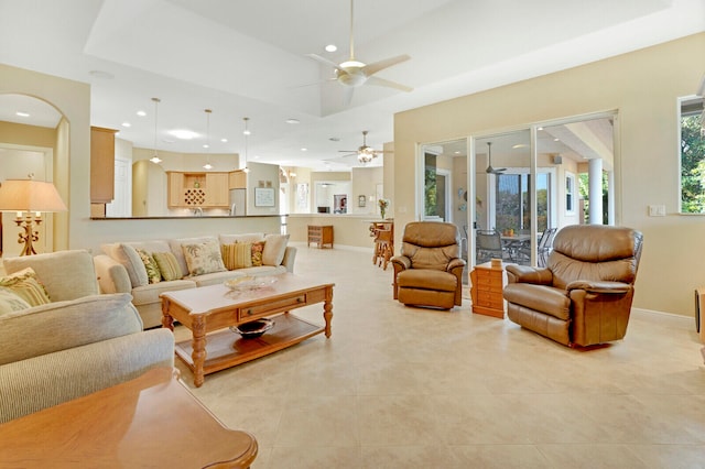 living room featuring a raised ceiling, ceiling fan, and light tile patterned flooring