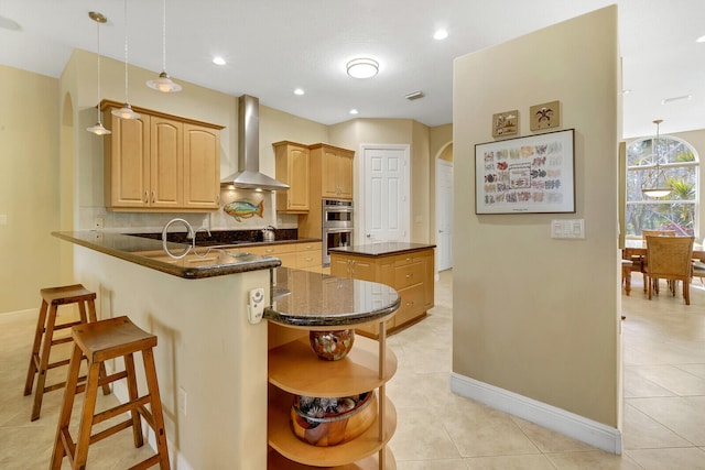 kitchen featuring a center island, wall chimney range hood, kitchen peninsula, decorative light fixtures, and stainless steel double oven