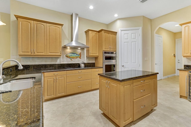 kitchen featuring appliances with stainless steel finishes, dark stone countertops, wall chimney exhaust hood, and sink