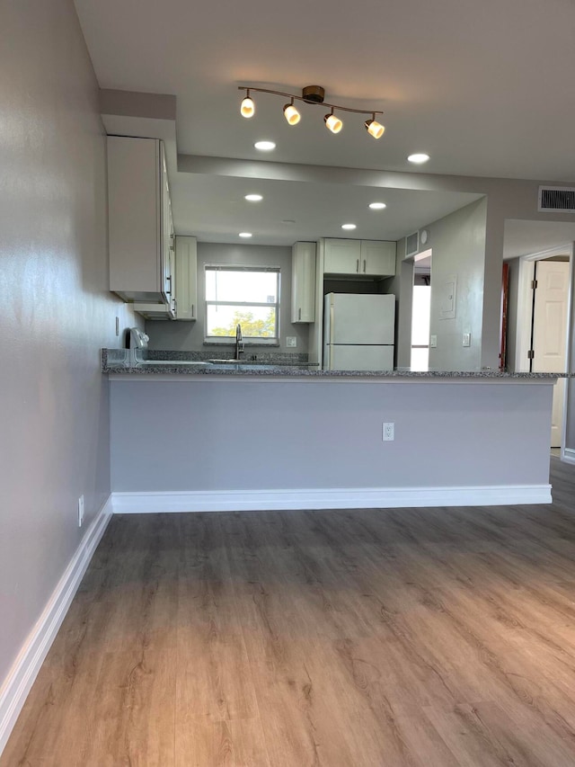 kitchen with kitchen peninsula, light stone countertops, white fridge, hardwood / wood-style flooring, and sink