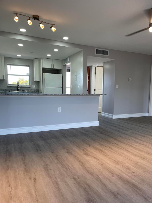 kitchen featuring light stone counters, white refrigerator, sink, kitchen peninsula, and wood-type flooring