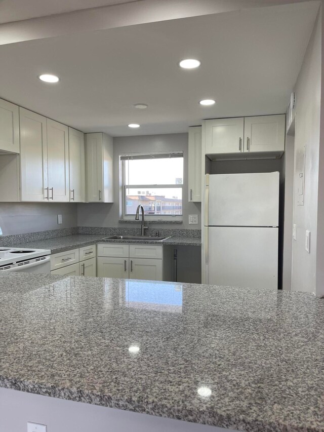 kitchen with white appliances, dark stone countertops, sink, and white cabinets