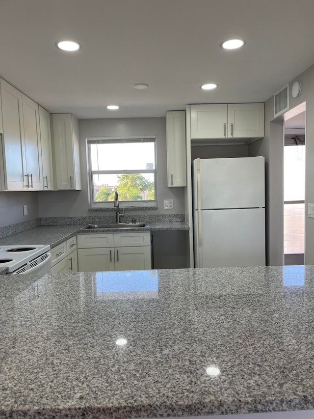 kitchen with dark stone counters, white appliances, white cabinetry, and sink