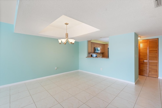 spare room featuring light tile patterned flooring, a textured ceiling, a tray ceiling, and a chandelier