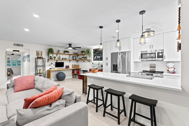 kitchen featuring appliances with stainless steel finishes, hanging light fixtures, white cabinetry, a kitchen bar, and ceiling fan