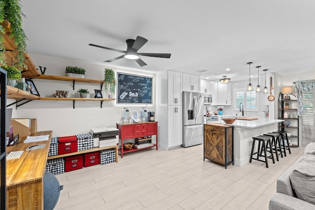 kitchen featuring white cabinetry, a kitchen bar, appliances with stainless steel finishes, decorative light fixtures, and ceiling fan