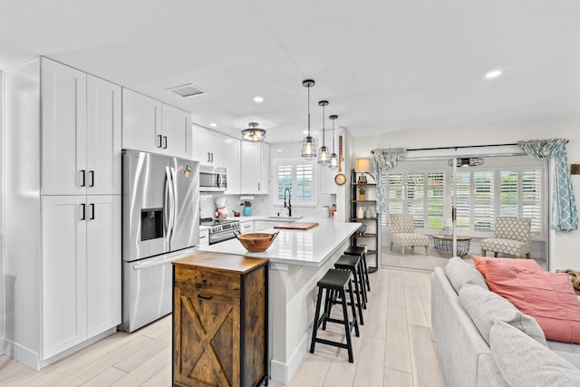 kitchen with a kitchen island, decorative light fixtures, white cabinetry, stainless steel appliances, and light wood-type flooring