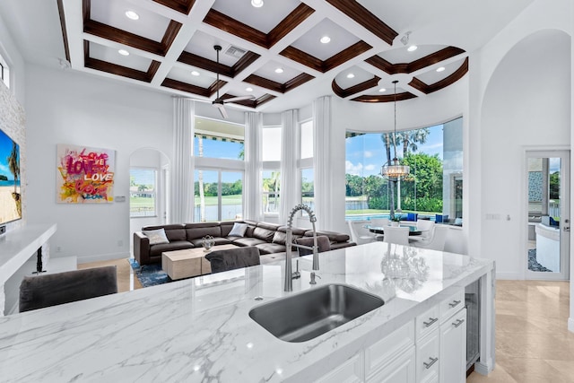 kitchen with beamed ceiling, sink, white cabinetry, light stone countertops, and a high ceiling