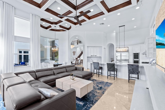 living room with ceiling fan with notable chandelier, beam ceiling, coffered ceiling, and a towering ceiling