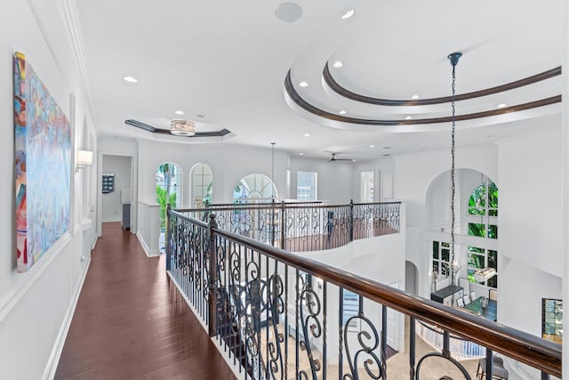 hall featuring an inviting chandelier, a tray ceiling, crown molding, and dark wood-type flooring