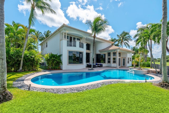 back of property featuring a lawn, a balcony, a swimming pool with hot tub, and a patio area