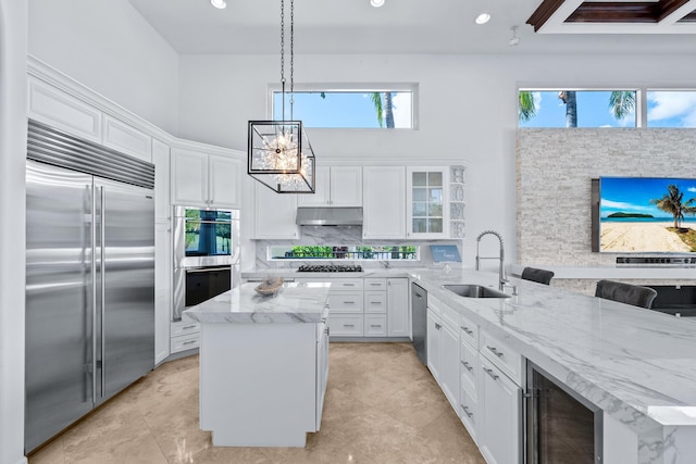 kitchen with appliances with stainless steel finishes, wine cooler, white cabinets, decorative light fixtures, and sink