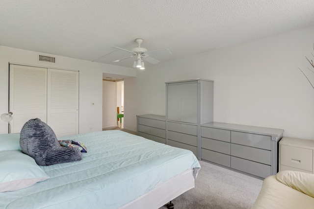 bedroom featuring ceiling fan, light colored carpet, a textured ceiling, and a closet