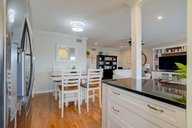 kitchen featuring dark stone counters, light wood-type flooring, white cabinetry, stainless steel refrigerator, and ornamental molding