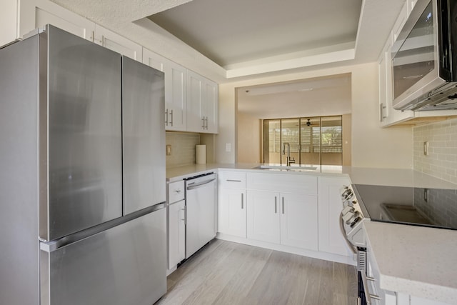 kitchen with sink, tasteful backsplash, white cabinetry, stainless steel appliances, and light hardwood / wood-style floors