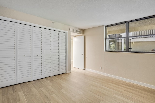 unfurnished bedroom featuring a textured ceiling, light hardwood / wood-style flooring, and a closet