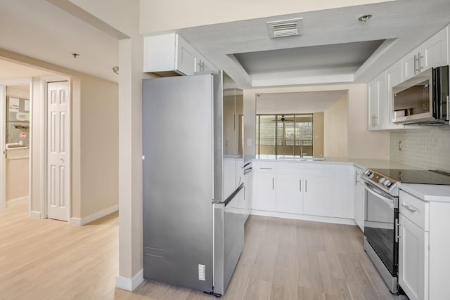 kitchen with light wood-type flooring, white cabinetry, stainless steel appliances, and tasteful backsplash