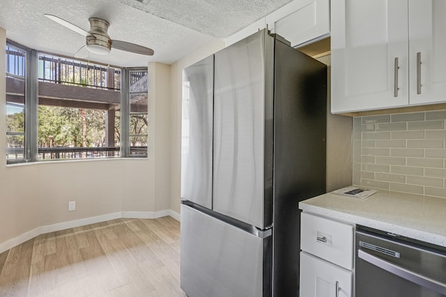 kitchen featuring appliances with stainless steel finishes, tasteful backsplash, white cabinets, light stone countertops, and light wood-type flooring