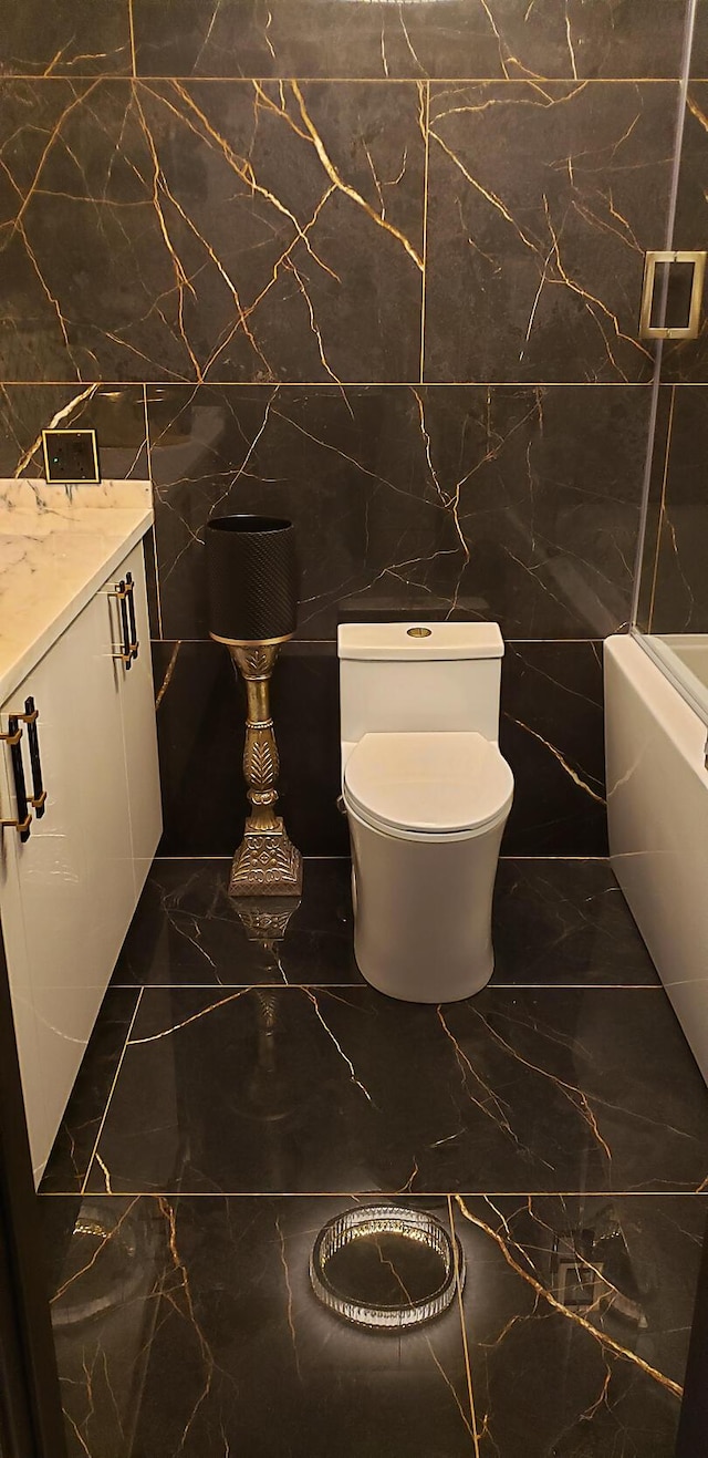 bathroom featuring vanity, toilet, a tub to relax in, and tile walls