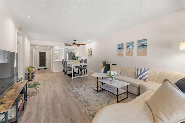 living room featuring ceiling fan, a textured ceiling, and light hardwood / wood-style flooring