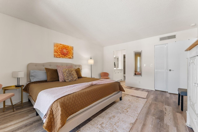 bedroom featuring ensuite bathroom, hardwood / wood-style floors, and a textured ceiling