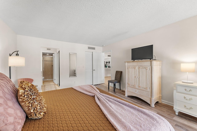 bedroom with light wood-type flooring, connected bathroom, and a textured ceiling