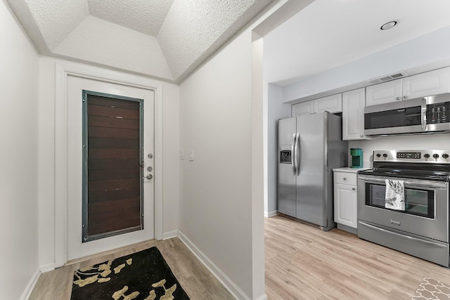 kitchen with appliances with stainless steel finishes, a textured ceiling, white cabinetry, and light hardwood / wood-style flooring