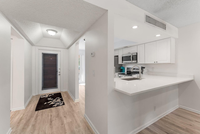 kitchen featuring light hardwood / wood-style floors, white cabinetry, kitchen peninsula, vaulted ceiling, and appliances with stainless steel finishes