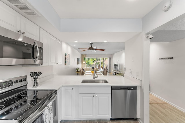 kitchen with white cabinets, sink, kitchen peninsula, light hardwood / wood-style flooring, and appliances with stainless steel finishes