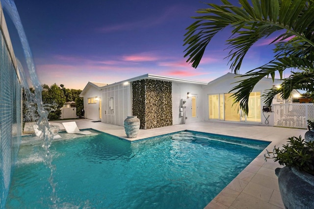 pool at dusk featuring pool water feature and a patio area