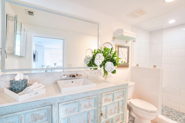 bathroom with toilet, a tile shower, tile walls, and vanity