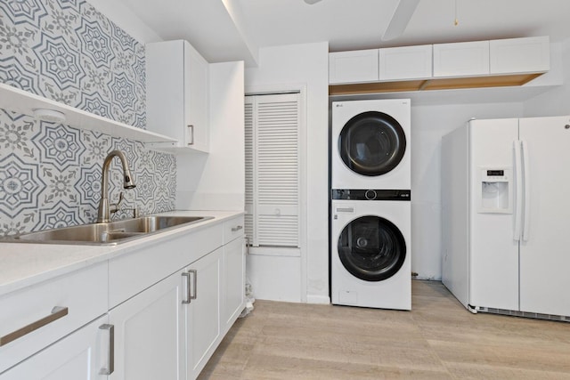 washroom with stacked washing maching and dryer, ceiling fan, light wood-type flooring, and sink