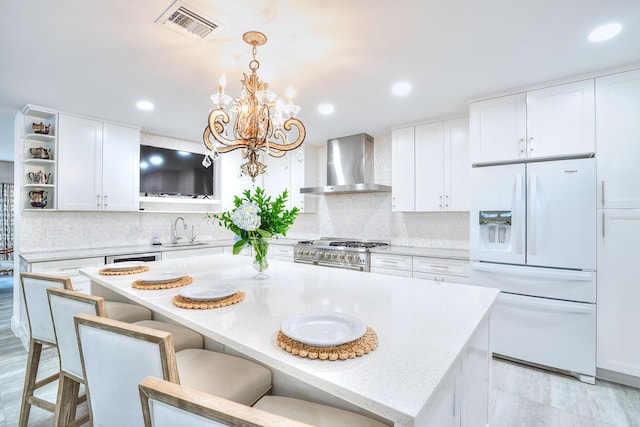 kitchen with white cabinetry, wall chimney range hood, white fridge with ice dispenser, and decorative light fixtures