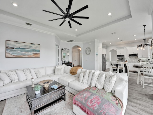 living room featuring ceiling fan with notable chandelier, ornamental molding, light hardwood / wood-style flooring, and a raised ceiling