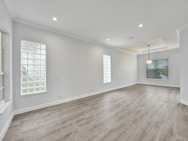 empty room featuring light wood-type flooring, ornamental molding, and a tray ceiling