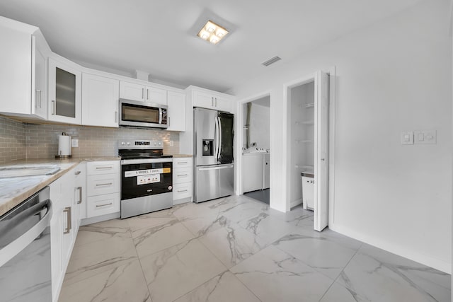 kitchen with light stone countertops, decorative backsplash, separate washer and dryer, stainless steel appliances, and white cabinets