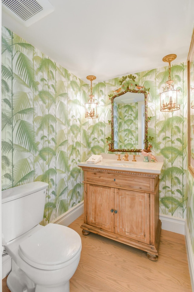 bathroom featuring a notable chandelier, hardwood / wood-style floors, vanity, and toilet