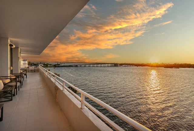 balcony at dusk featuring a water view