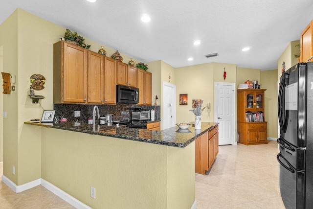 kitchen featuring dark stone countertops, black appliances, kitchen peninsula, and tasteful backsplash