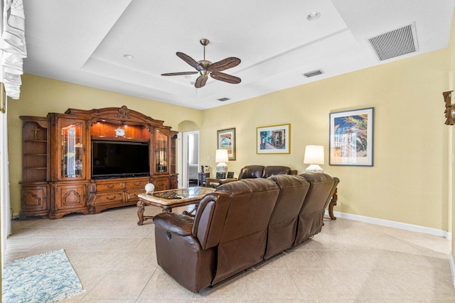 living room with ceiling fan, a raised ceiling, and light tile patterned floors