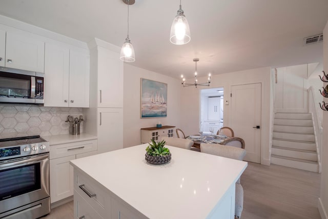 kitchen featuring light wood-type flooring, pendant lighting, backsplash, white cabinets, and appliances with stainless steel finishes