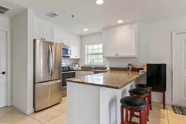 kitchen with appliances with stainless steel finishes, kitchen peninsula, a kitchen bar, and white cabinets