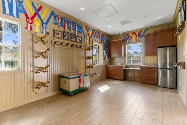 kitchen featuring stainless steel fridge, light hardwood / wood-style flooring, crown molding, and wooden walls