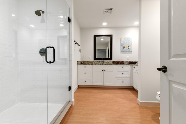 bathroom featuring vanity, toilet, wood-type flooring, and a shower with door