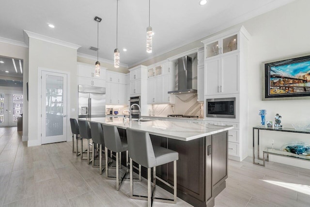 kitchen with pendant lighting, white cabinets, a large island with sink, and wall chimney range hood