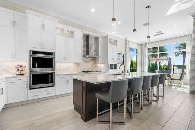 kitchen featuring appliances with stainless steel finishes, a center island with sink, white cabinetry, and wall chimney range hood