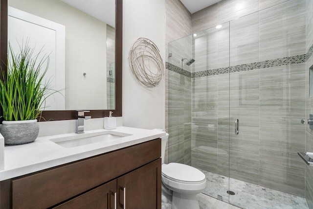 bathroom featuring a shower with shower door, vanity, and toilet