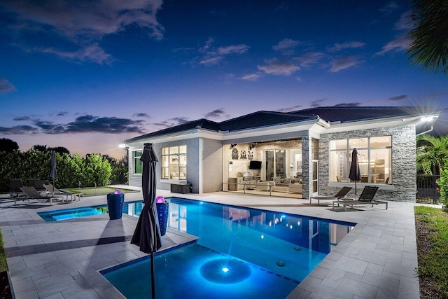 pool at dusk featuring a patio, an outdoor living space, and a jacuzzi