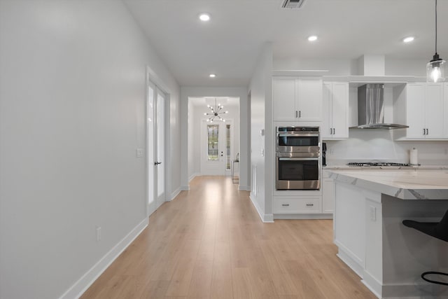 kitchen featuring stainless steel appliances, white cabinets, light hardwood / wood-style floors, wall chimney range hood, and decorative light fixtures